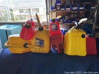Nine assorted jerry cans in red, yellow, and orange plastic arranged on a blue surface indoors.