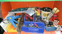 Wide shot of various tools and hardware in orange plastic bin including caulking gun, saw, screwdrivers, and packages of washers