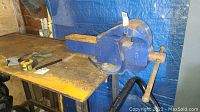 Side angle showing the blue metal Eron No 150 vise mounted on a metal bench, with visible rust and spiral handle for operation.