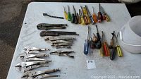 Wide view of all vise grips and screwdrivers on table.