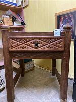 Front view of wooden side table showing carved geometric pattern on drawer and ring metal handle.