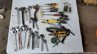 Overview of the collection of tools spread on a white surface showing wrenches, screwdrivers, and other hand tools with some rust visible.