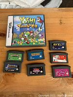 Nintendo DS game Yoshi Touch & Go case and seven Game Boy Advance cartridges laid out on wooden surface