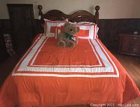 Full view of wooden bed frame with mattress, orange and white bedding, and teddy bear on top showing the overall look and condition