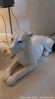 Side view of large white ceramic cat sculpture laying on floor, showing posture and glossy finish