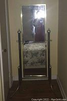 Full-length view of the metal cheval mirror showing its rectangular reflective surface, metal frame, and base structure with finial detailing on the posts.