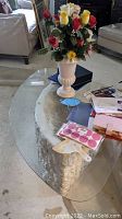 Cement coffee table with decorative flower vase and various items on glass top, showing the overall look and usage.