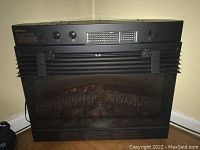 Front view of black Dimplex electric fireplace, showing simulated log fire inside and control knobs on top panel.