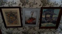 Three framed prints laid out on floral fabric showing different scenes and varied frames.