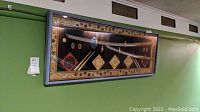 Wide view of the framed display containing two Asian sabers and many decorative tiles.