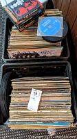 Black plastic crates containing a large number of vinyl records with DVDs and CDs placed on top. Visible album covers include a compilation with The Platters.