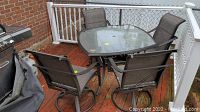 Full view of the patio set showing the table and four chairs arranged on a wooden deck with a grill nearby.