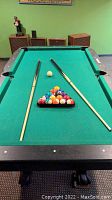 Two pool cues laid on a green felt pool table with pool balls racked in triangle form in the center of the table.