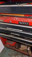 Close-up photo of red Husky metal tool cart drawer face with brand label and paint splatters showing wear and oxidation.