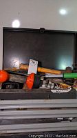 Top view of tool chest lid opened, showing various loose tools on top including a wooden handled hammer and red plastic knobs on tools.