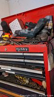Red Husky metal toolbox with multiple drawers, some tools visible on top and inside drawers.