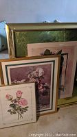 Three floral wall art pieces shown leaning together, varying sizes and frames visible including gilded border on largest piece.