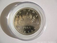 Photo of 1965 Canadian one dollar silver coin showing canoe design, encased in a clear plastic capsule for protection.