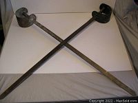 Two heavy metal prop swords crossed on a white surface, showing overall length and hand guard design.