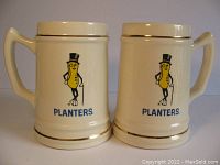Front and side view of two cream-colored ceramic stein mugs with Mr. Peanut graphics and gold trim, showing handles and logo