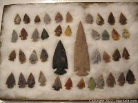 Entire set of 40 small notched arrowheads and 2 larger spearheads arranged on white padding.