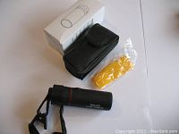 Overview of the monocular telescope laid flat alongside the black storage pouch, white box, and sealed yellow cleaning cloth.