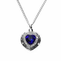 Silver toned heart-shaped pendant urn with large blue simulated sapphire and smaller white simulated sapphires pendant on a chain against a white background.