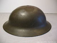 Side view of olive drab basin-shaped steel helmet with some surface wear and dents.