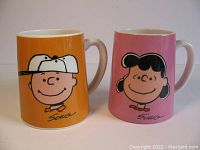 Front view showing Charlie Brown on orange mug and Lucy on pink mug, signed Schulz