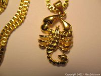 Close-up view of gold plated scorpion pendant showing detailed claws, body, and tail with attached ring for chain.