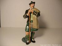 Front-facing view of the Royal Doulton The Laird porcelain figurine in traditional Scottish attire with walking stick.