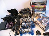 Two PlayStation 2 horizontal consoles with six controllers and 21 games, all displayed with open disc trays, visible cables, and game cases.