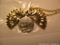 Close-up of the opened sunflower locket showing the engraved message 'You Are My Sunshine' on the disk inside.