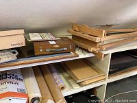 Wooden shelving with art supplies including easels, rolls of paper, framed canvases, and a wooden box.