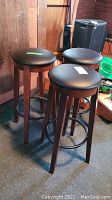 Three dark wood and metal bar stools with circular black padded seats, showing wear on legs and frames.