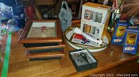 Overview of lot items on wooden table including framed plaques, packaged glasses, bar trays, boxed sets, and bar tap handles.