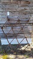 Full front view of vintage metal chain harrow with diamond lattice structure leaning against wooden wall.