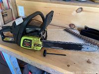 Side view of Poulan Wood Shark chainsaw on a wooden surface, showing the full 14-inch bar and chain, pull starter handle on table.