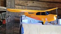 Yellow and orange styrofoam model airplane on cardboard box showing side and top view of wings and cockpit.