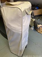 Beige fabric carry case for folding bed frame and mattress with handle shown.