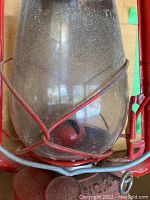 Close-up of dusty glass globe and red metal frame of kerosene lamp