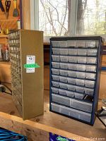 Photo of two metal storage organizers, one green and one black, on a workbench showing multiple rows of clear plastic drawers.