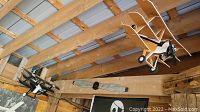 Two unfinished black and white wooden triplane models hanging from wood beam with rustic support prop below