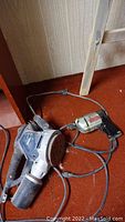 Both power tools shown on a carpeted floor, including Rina Magnesium electric sander and Black & Decker drill with cords.