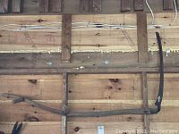 Full length view of the antique scythe showing the wooden handle and curved metal blade against a wood background.