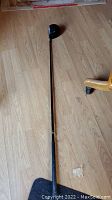 Full length view of the golf driver showing the clubhead, shaft, and grip on a wooden floor.