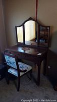 Wooden vanity table with attached triple mirror and two front drawers, dark wood finish, showing surface wear.