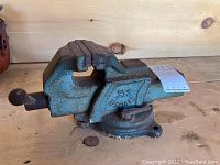 Side view of Hercules bench vice showing entire body and rotating base attachment; the vice is mounted on a wooden surface.