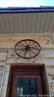 Front view of the metal wagon wheel mounted above a door on a wood wall, showing overall shape and condition.