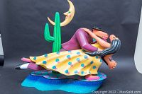 Side view of entire painted sculpture showing dancing couple, cactus and moon against dark backdrop.